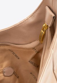 Interno della borsa in pelle color beige con una consistenza liscia, caratterizzato da una zip dorata e foderato con un marchio in stampa scura.