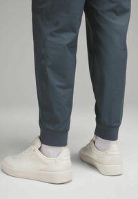 Sportowe joggery w ciemnoniebieskim kolorze z prążkowanym mankietem, zestawione z jasnobeżowymi sneakersami o gładkiej teksturze i subtelnym detalem logo.