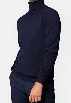 Marineblauer Rollkragenpullover aus Rippstrick, mit einer taillierten Silhouette, langen Ärmeln und einem dezenten Logo auf der Brust.