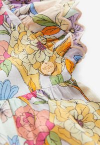 Tessuto a fantasia floreale in colori pastello con bordi arricciati e un dettaglio in forma di bottone circolare dorato, caratterizzato da un'incisione floreale.