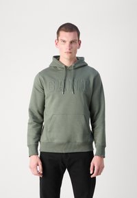 Sudadera verde oliva con bolsillo canguro, capucha con cordón y logo "GANT" grabado en el pecho. Puños y dobladillo acanalados.