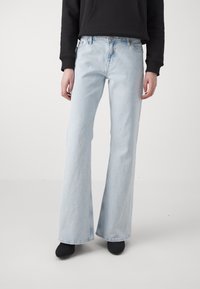 Světle modré zvonové džíny vyrobené z denimu, s vysokým pasem, předními kapsami a viditelným švem. Nosené s černými kotníkovými botami.