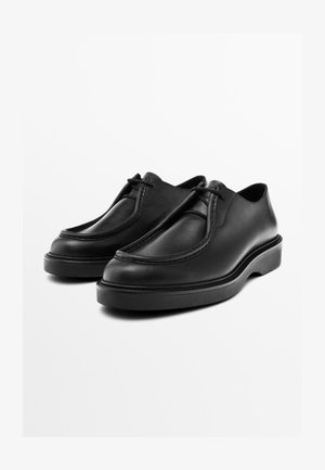 Schwarze Lederschuhe mit abgerundetem Zehenbereich, gesteppten Akzenten und einer flachen Plattformsohle. Ausgestattet mit einer glatten Oberfläche und minimalem Schnürdetail.