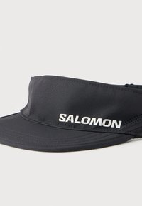 Μαύρο αθλητικό καπέλο τύπου visor της Salomon με καμπυλωτό γείσο και λευκό λογότυπο στη μπροστινή ταινία, σε απλό λευκό φόντο.