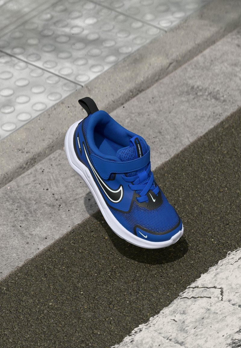 Modrá sportovní bota vyrobená z prodyšné síťoviny a gumy, s černými detaily, bezpečným páskem a bílou podrážkou s texturovanými vzory.