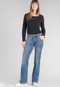 Blue denim flared jeans with a faded wash, featuring front pockets and a button closure, paired with a black long-sleeve top.