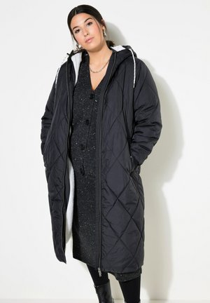 Black quilted long coat with a zipper, featuring a hood and white fleece lining. Worn over a dark textured dress and black tights.