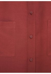 Camisa de botonadura en color óxido con tejido texturizado, que presenta un cuello y dos bolsillos en el pecho. Los botones coinciden con el color de la tela.