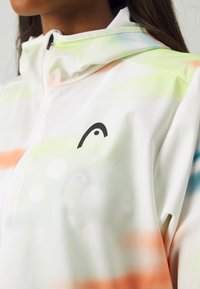 Lightweight, white jacket with multicolor gradient patterns. Features a high collar, zip closure, and a black logo on the chest.