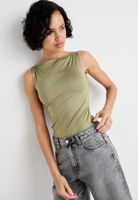 Olivenfärgad, ärmlös bodysuit med en axel-design, i kombination med högmidjade, slitna grå jeans. Slät textur, åtsittande siluett.