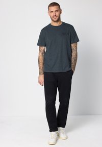 Tmavě šedé bavlněné tričko s kulatým výstřihem, krátkými rukávy a malým černým potiskem na hrudi, doplněné černými kalhotami a bílými teniskami.