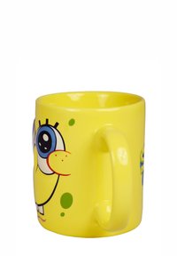Mug in ceramica gialla con un personaggio dei cartoni animati con grandi occhi blu e un sorriso prominente. Texture liscia con forma arrotondata e manico.
