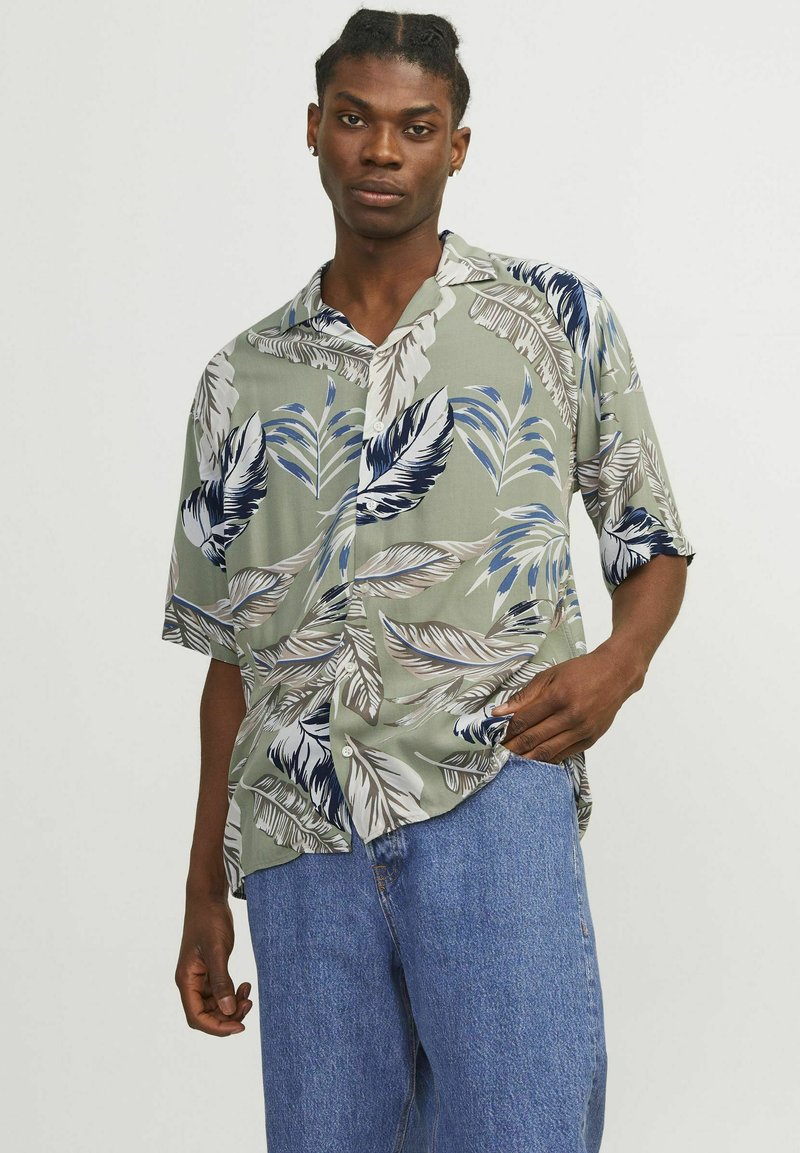 Camisa de manga corta abotonada en verde claro con grandes patrones de hojas azules y marrones. Fabricada con tela suave; corte relajado con cuello.