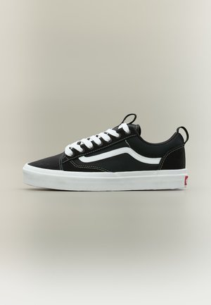 Μαύρο χαμηλό sneaker με λευκή σόλα, λευκά κορδόνια, λευκή πλαϊνή ρίγα και μαύρες θηλιές στην γλώσσα και στη φτέρνα.