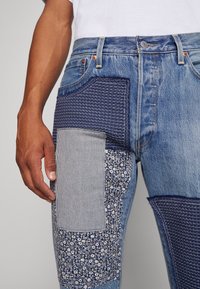 Džínové kalhoty s několika panely patchwork v různých modrých tónech, se květinovými a pruhovanými vzory, a klasickým pěti-kapsovým designem.