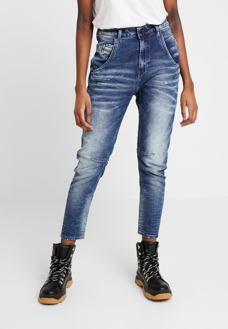 Höga jeans i medelblått denim med blekta områden, avsmalnande ben och femfickorsdesign, ihop med svarta snörstövlar.