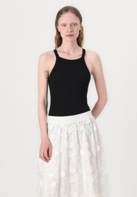 Zwarte mouwloze top met hoge hals, gecombineerd met een witte doorschijnende rok met textuur en bloemenborduurwerk en een elastische tailleband.