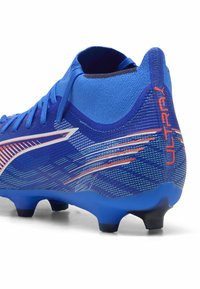 Scarpa da calcio blu con tomaia testurizzata e dettagli arancioni e bianchi, tallone sagomato e tacchetti in plastica nera per una migliore aderenza.