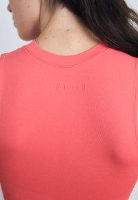 Top fără mâneci de culoare corai cu decolteu rotund, fabricat dintr-un material neted; are un logo „Calvin Klein” embosat pe spate.