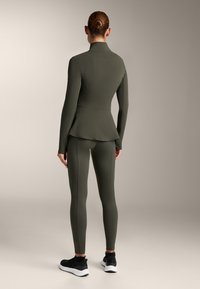 Olive green activewear set featuring a fitted jacket with a peplum design and matching leggings. The outfit has a smooth texture and minimal detailing.