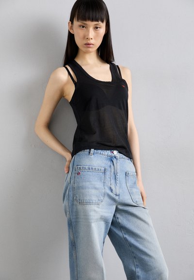 Top cu bretele subțiri, de culoare neagră și transparent, cu un logo roșu, asortat cu blugi din denim de un albastru deschis, cu buzunare la spate și o textură ușor decolorată.