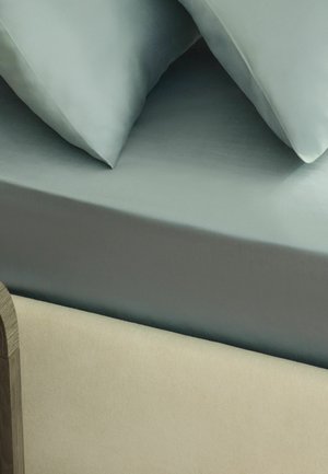 Zwei hellblaue Kissen auf einem ordentlich gemachten Bett mit passendem hellblauen Laken und beigem gepolstertem Bettrahmen.