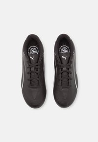 Scarpe sportive nere con tomaia sintetica liscia, dettagli bianchi e lacci piatti. Punta arrotondata e rivestimento imbottito per il comfort.