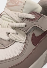 Κοντινή λήψη μπεζ και κρεμ αθλητικού παπουτσιού Nike με λευκά κορδόνια, υφασμάτινη υφή και λογότυπο Nike σε σκούρο μπεζ χρώμα στη πλευρά.