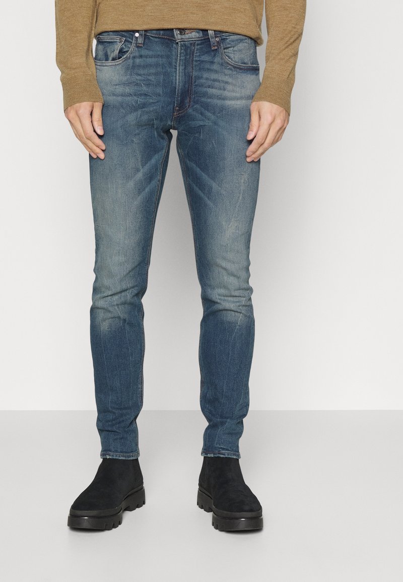 Slim-fit modré džíny vyrobené z denimu, s bledým povrchem, pěti-pocket designem a kontrastním šitím, spárované s černými semišovými botami.