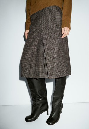 Jupe à carreaux marron avec des plis, fabriquée à partir d'un tissu texturé. Associée à des bottes en cuir noir à talons, arrivant au genou. Design simple et structuré.