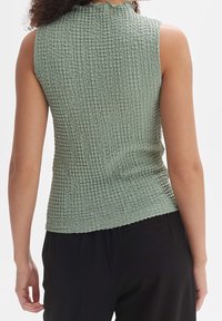 Zelený top bez rukávů s texturou, s vroubkovaným výstřihem, provedený z nařasené tkaniny a s přiléhavým střihem.