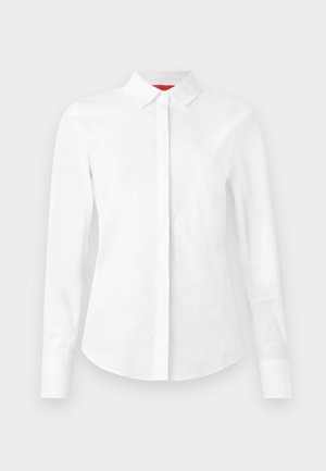 Camicia bianca a maniche lunghe con colletto a punta, placca di bottoni nascosta e vestibilità su misura, su uno sfondo semplice.