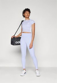 Haut de sport court violet clair et leggings taille haute assortis. Sac noir avec logo "adidas" blanc. Tissu texturé, design sportif.