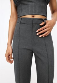 Pantalon gris sur mesure avec une texture lisse, doté d'une taille ajustée, de poches latérales et de plis subtils à l'avant.