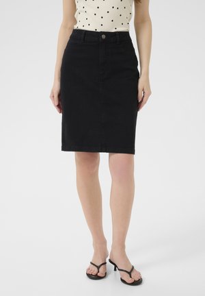 Jupe crayon en denim noir avec une taille mi-haute, des poches avant et une coupe droite, associée à des sandales noires à bout ouvert.