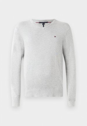Svetlo sivi pulover iz pletene tkanine, z V-izrezom, dolgimi rokavi in majhnim logotipom na prsih. Gladka tekstura.