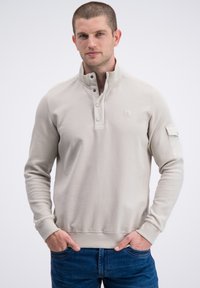 Lichtbeige pullover met gestructureerde schouderpanelen, kraag met drukknoopsluiting en geribbelde manchetten. Voorzien van een klein logo op de borst.
