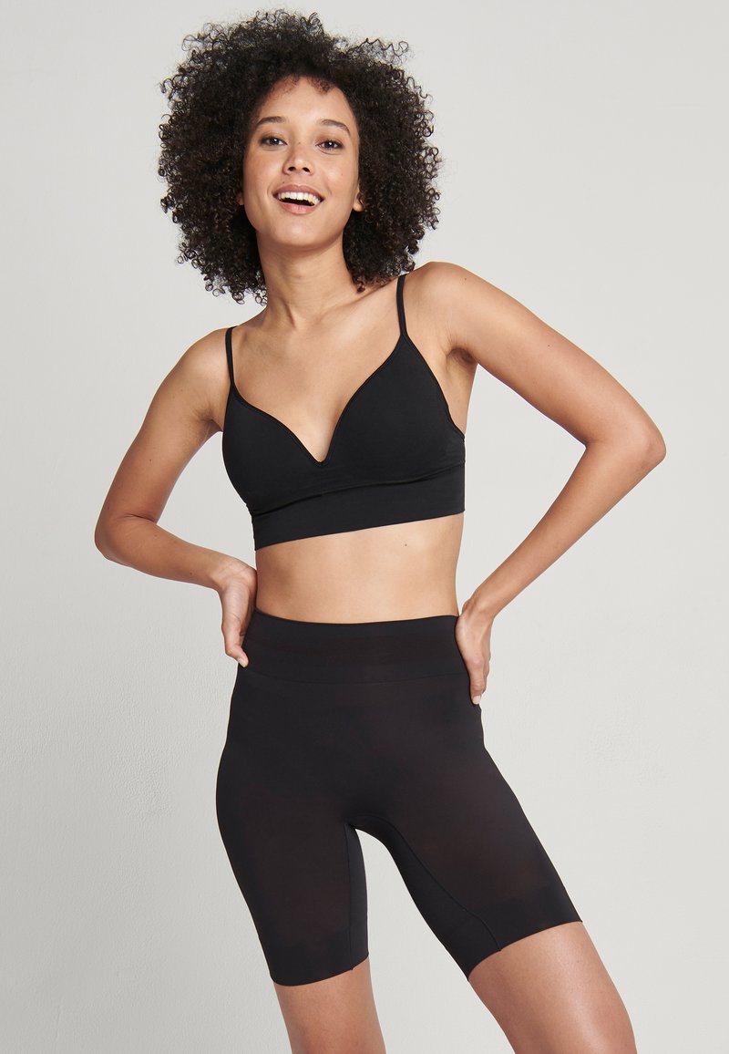 Svart bralette med V-ringad design och tunna band, kombinerad med högmidjade svarta cykelshorts. Slät textur, åtsittande passform, inga synliga mönster.