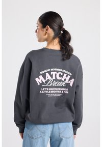 Sweat-shirt gris surdimensionné en coton avec texte blanc et rose au dos, doté d'un design incurvé et d'une coupe décontractée.