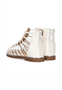 Botas de tobillo de imitación de cuero blanco con un diseño de tiras, cremalleras traseras y suela marrón. Presenta acentos metálicos a lo largo del borde.