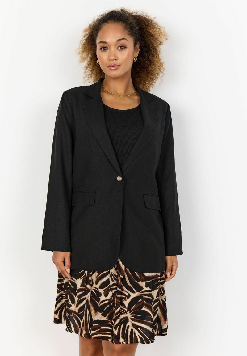 Schwarzer Blazer mit strukturiertem Design, Reverskragen und zwei Vordertaschen, kombiniert mit einem gemusterten Rock in Braun und Creme mit Blattmotiven.