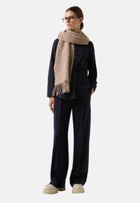 Marineblauwe twee-delige outfit met een knoopshirt en wijde broek, aangevuld met een beige sjaal met een visgraatpatroon en chunky beige schoenen.