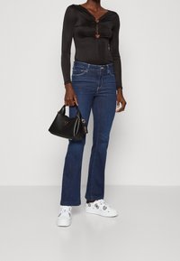 Musta pitkähihainen bodysuit, jossa on sydämenmuotoisia aukkoja, yhdistettynä tummansinisiin leveälahkeisiin farkkuihin ja valkoisiin lenkkareihin, joissa on mustia kuvioita; kädessä musta laukku.