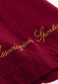 Bordeaux stof met een zachte textuur, voorzien van gele geborduurde tekst "Associazion. Sport" nabij de zoom.