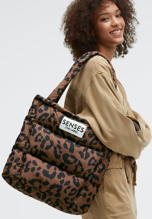 Brown leopard print tote bag with a padded design and a black label reading "SENSES THE LABEL." The strap is wide and patterned.