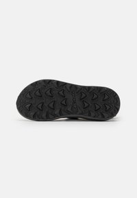 Suela de zapato de goma negra con patrones de textura para agarre, con un logotipo visible cerca del centro y un borde ligeramente elevado.
