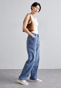 Jasnoniebieskie dżinsy z wysokim stanem o luźnym kroju, połączone z dopasowanym białym topem na ramiączkach i brązową zamszową torebką. Całość dopełniają białe trampki.