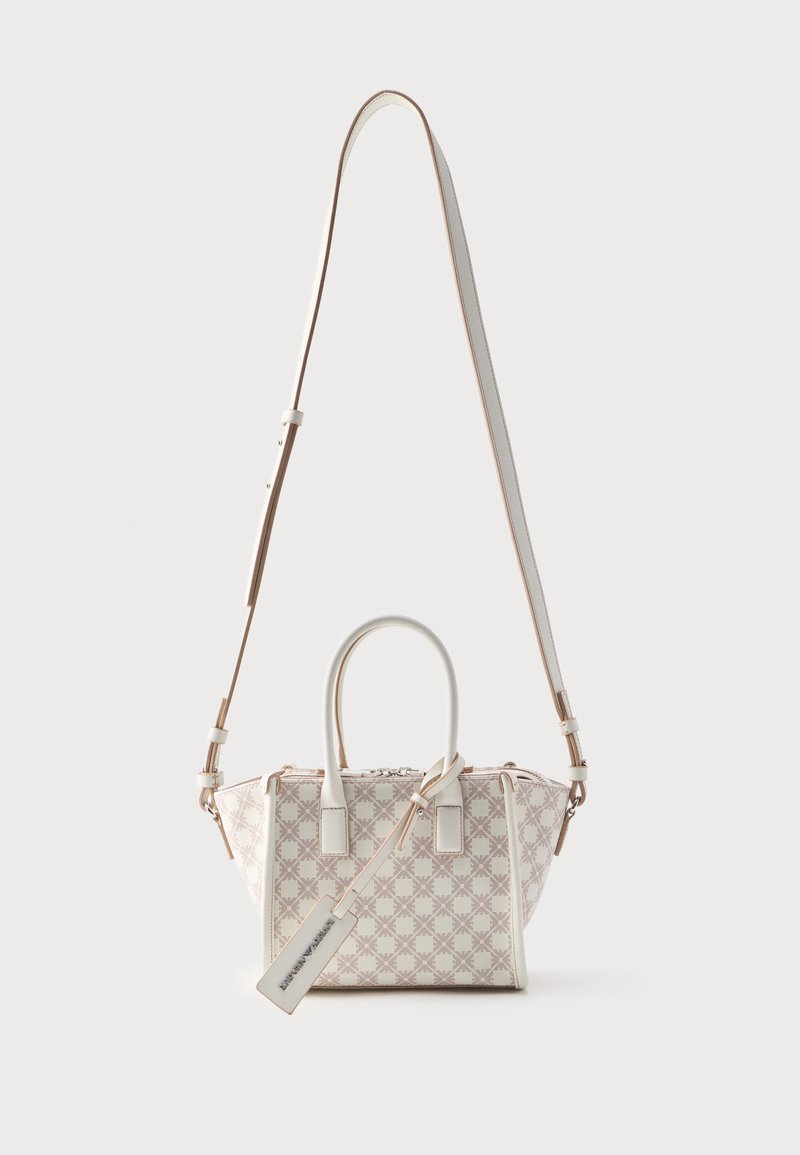 Μικρή μπεζ τσάντα χειρός με δύο κοντά χερούλια, μακρύ ρυθμιζόμενο λουρί ώμου και συνδεδεμένη ορθογώνια ετικέτα.