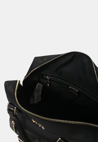 Zwarte tas met metalen hardware, met ritssluiting en stoffen voering. Het interieur bevat een zak met rits en zichtbare verzorgingslabels.