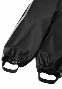 Czarne wodoodporne spodnie z elastycznymi mankietami i dwoma bocznymi paskami do zapięcia. Gładka faktura z odblaskowym paskiem wzdłuż boków.